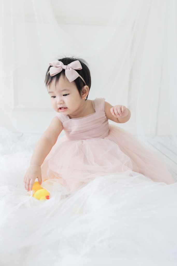 Close-up portrait of baby girl in pastel pink dress with natural soft lighting.