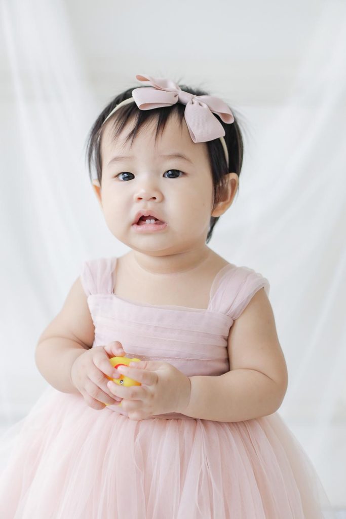 closed up Baby girl first birthday photoshoot wearing pastel pink dress holding rubber duckie