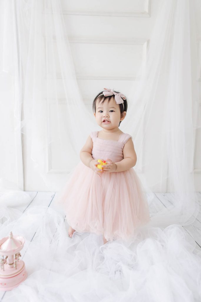 Baby girl first birthday photoshoot wearing pastel pink dress holding rubber duckie