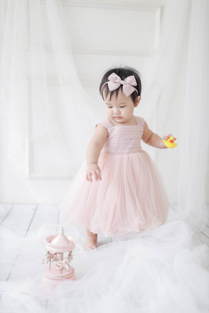 closed upBaby girl first birthday photoshoot wearing pastel pink dress holding rubber duckie